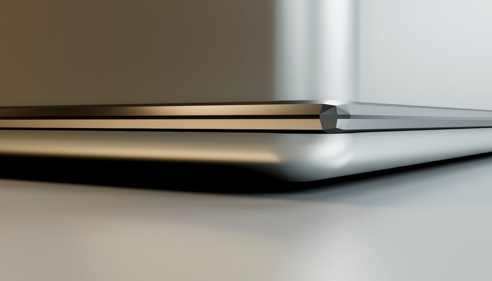 Closed laptop computer with a sleek metallic surface reflecting light on a smooth table.