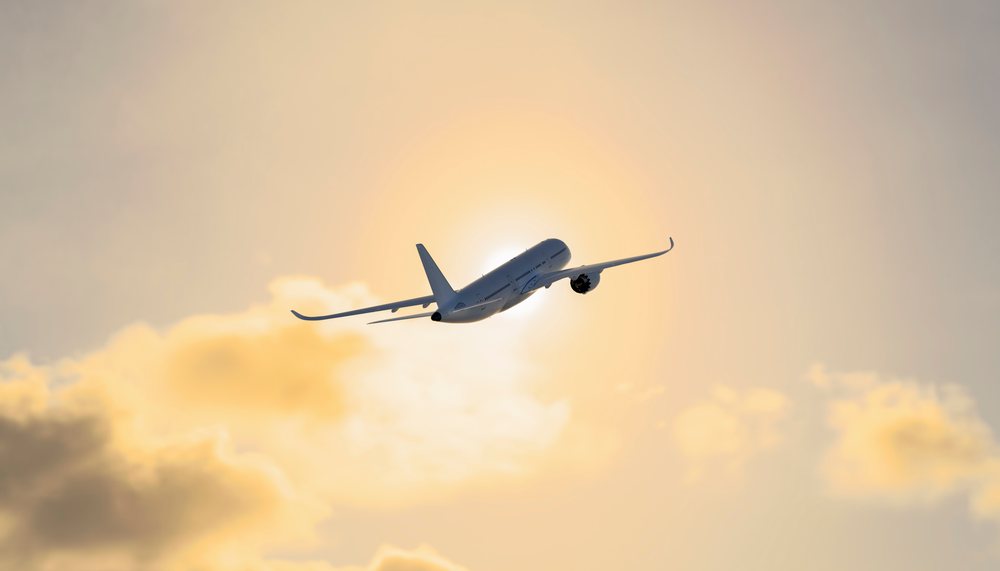 An airplane flying towards the sun through a partly cloudy sky at sunset, travel, fly, vacation.
