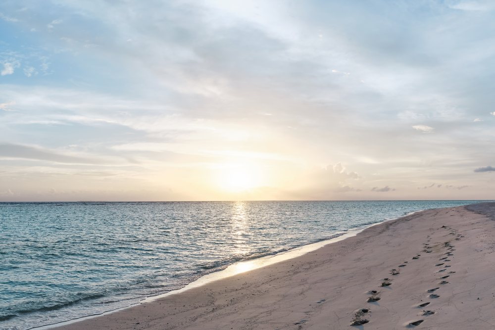 Sunset over a peaceful sandy beach with footprints in a beach