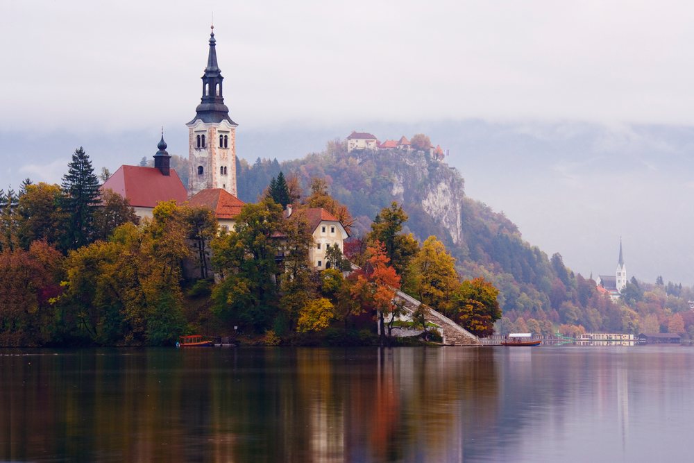 Church of Assumption on an island with autumn trees and misty mountains, Lake Bled, Slovenia.