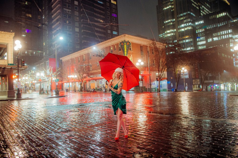 Woman in a green dress with red high heels holds a red umbrella on a wet brick street, boudoir, Seattle, USA.