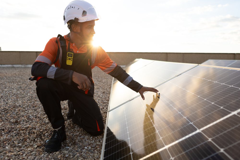 Man wearing a safety helmet inspects solar panels outdoors at sunset, Madrid, Spain.