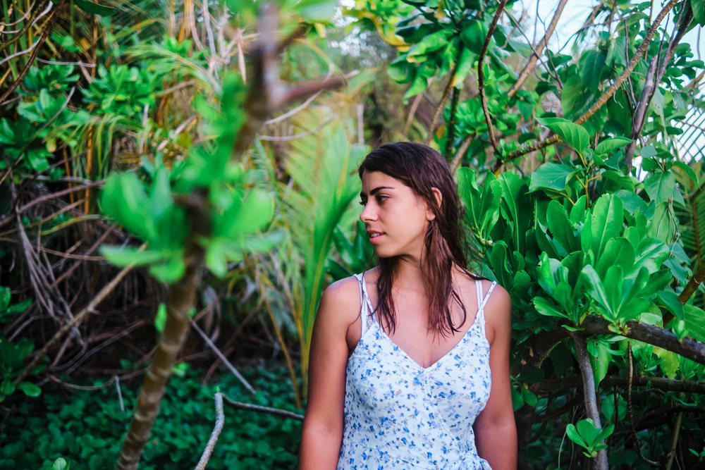 A woman in a floral summer dress stands among lush green tropical plants in the, Maldives.