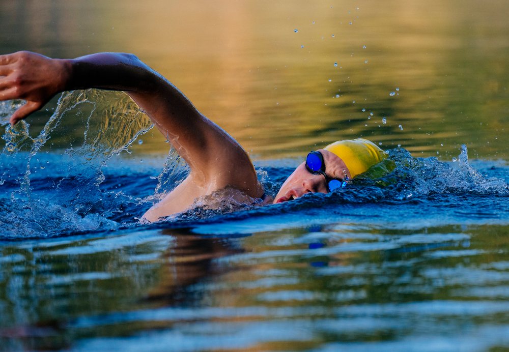Male swimmer wearing yellow swim cap and blue goggles performing a freestyle stroke in open water, USA.