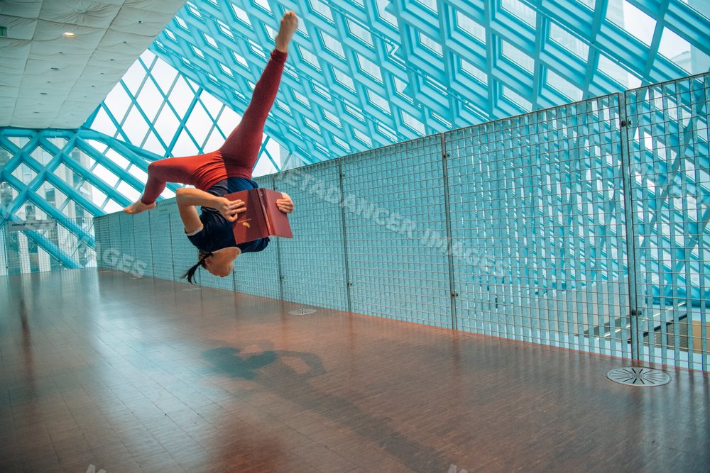 A woman performing a backflip while reading a book in a library