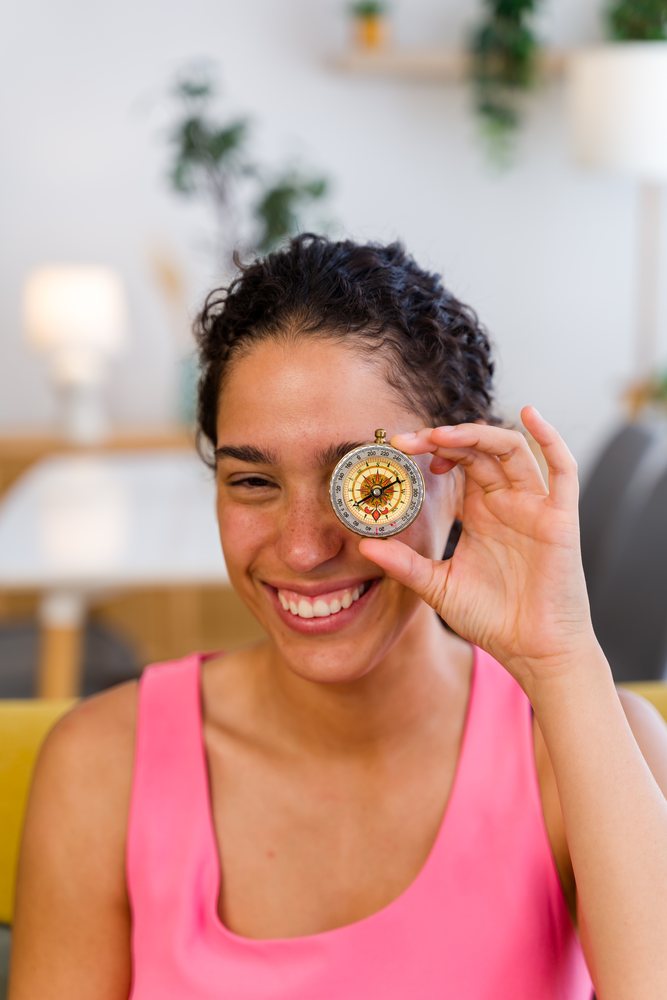 A smiling woman holds a compass in front of her eye indoors, Spain.