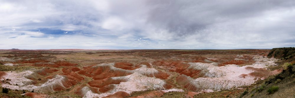 Painted Desert badlands show red and white rock formations under a cloudy sky, Arizona, USA.