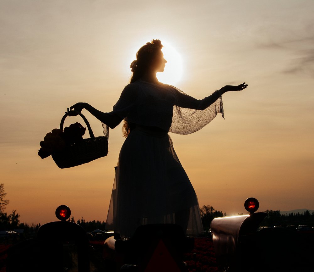 Silhouette of a woman holding a basket of flowers at sunset in a rural outdoor environment, USA.