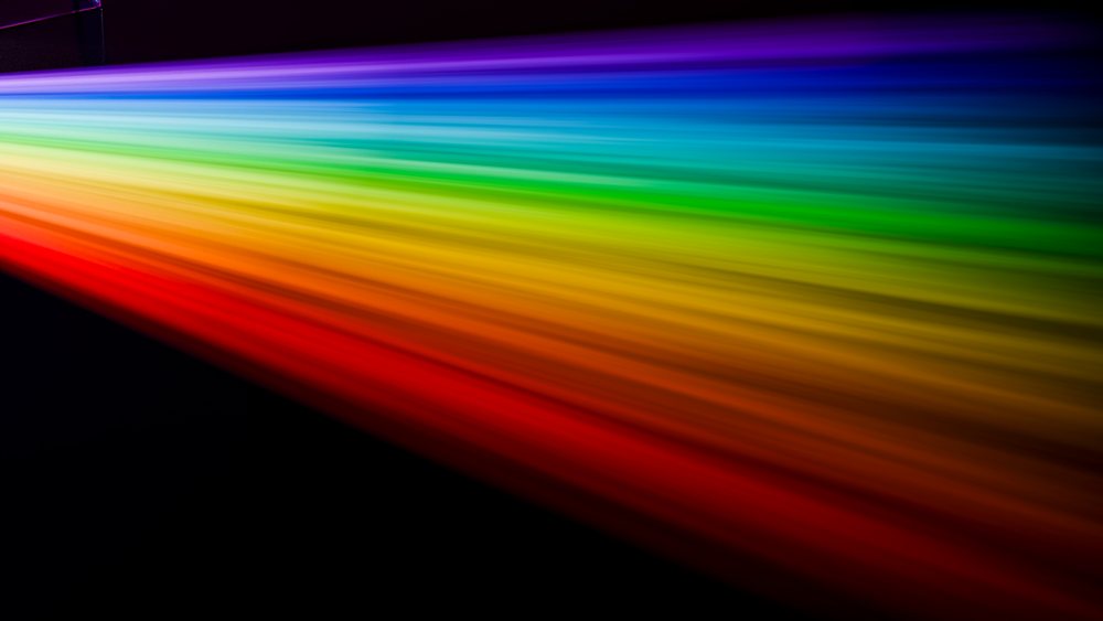 Rainbow light spectrum beam extending diagonally across black background with vibrant colors from violet to red.