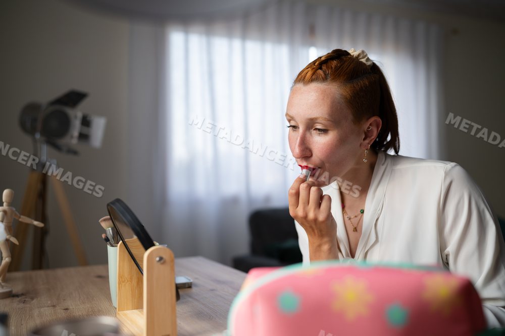 A white woman applies red lipstick
