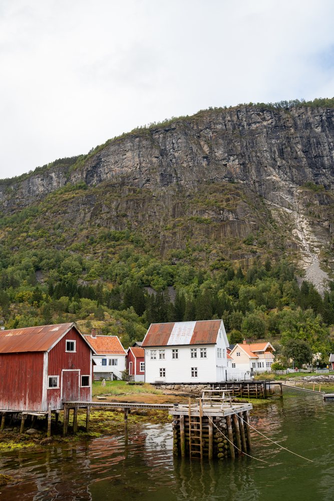 Norwegian Fjord village with wooden docks, rustic houses, and steep mountain cliffs reflected in calm water, coastal town, Luster, Norway.