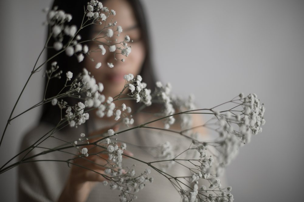 Portrait of a woman holding delicate white baby's breath flowers against a neutral indoor background, Art, emotional.