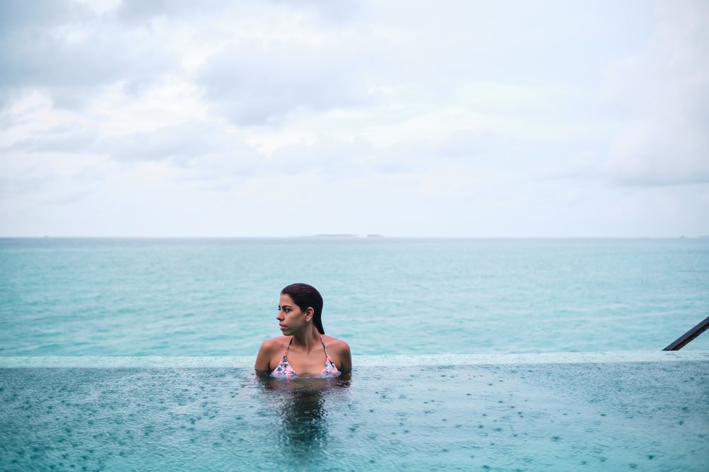 A white woman relaxing in an infinity pool overlooking the ocean