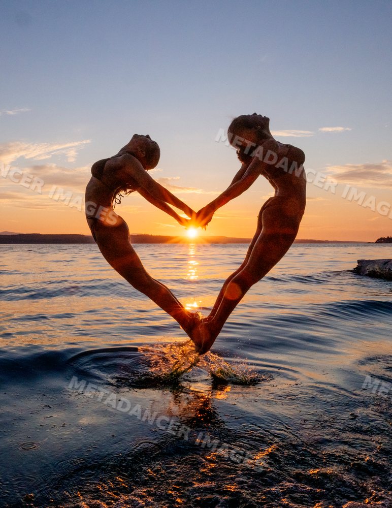 Two people doing partner acrobatics yoga jumping at sunset over water