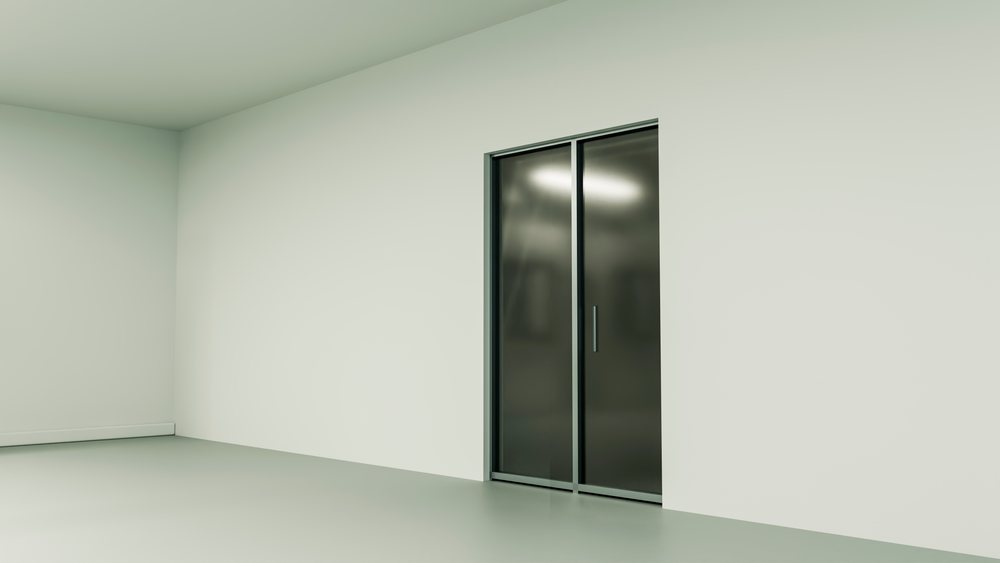 Modern glass sliding door with a door handle in an empty minimalist room with white walls and grey floor.