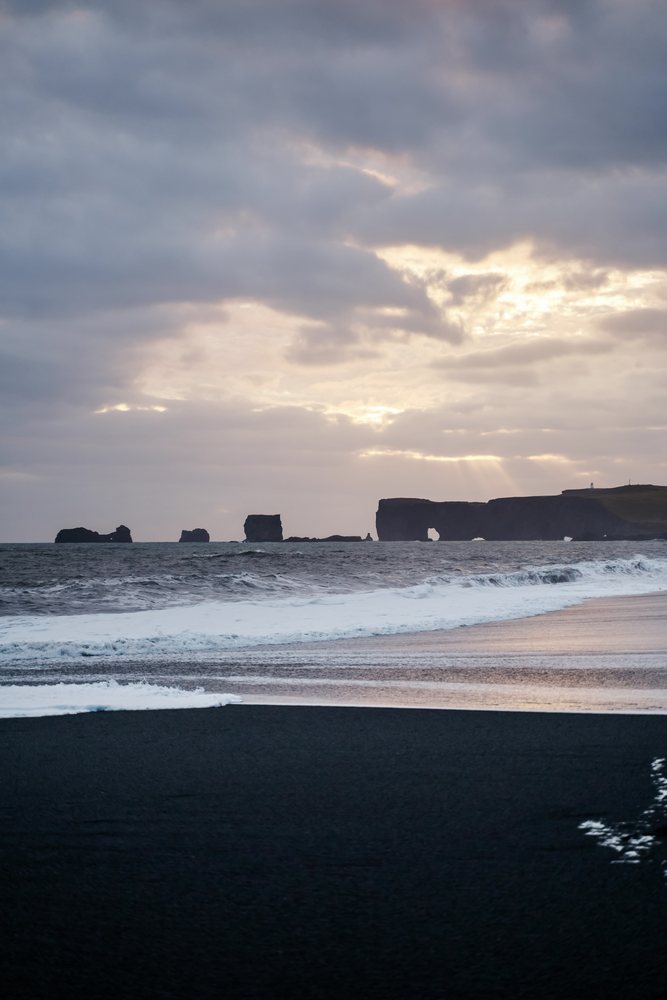 Ocean waves wash ashore on a black sand beach with sea stacks