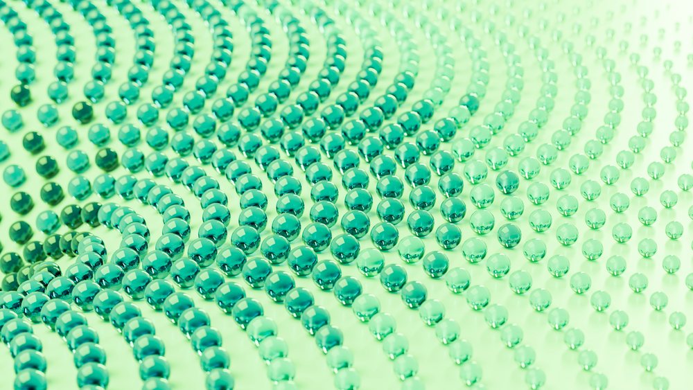 Numerous shiny green glass beads arranged in curved rows form an abstract decorative pattern on a flat surface.