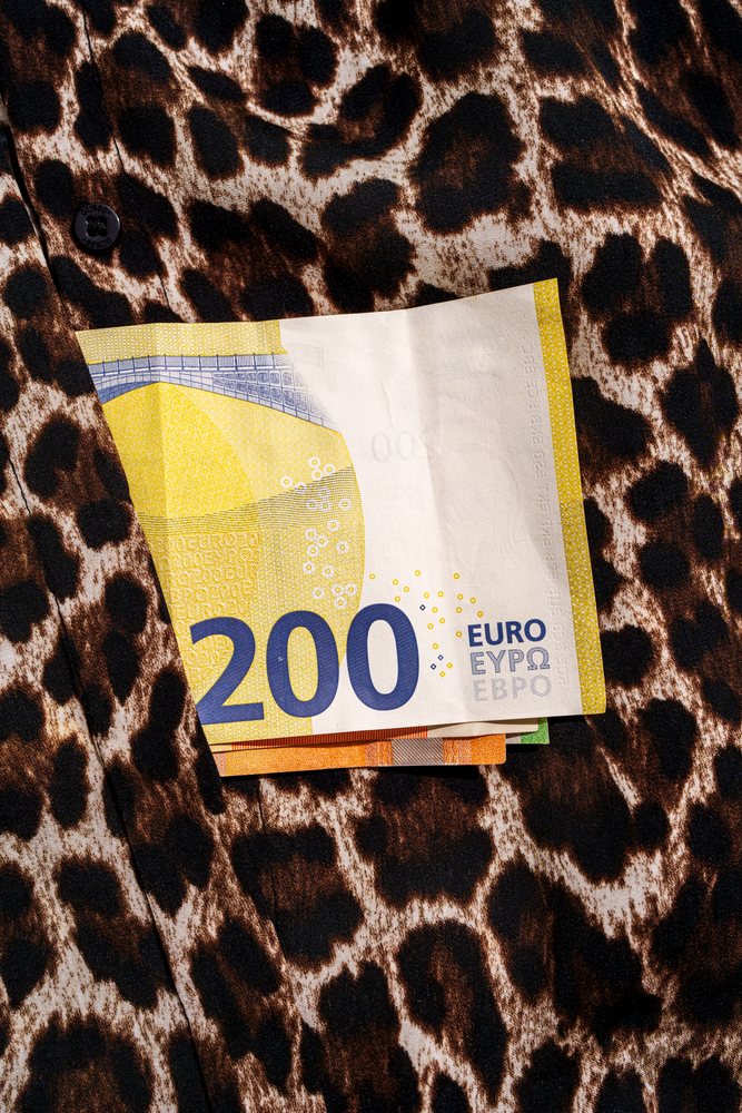 Folded 200 euro banknotes tucked into the pocket of a leopard print fabric garment in a studio setting, Studio Shot.