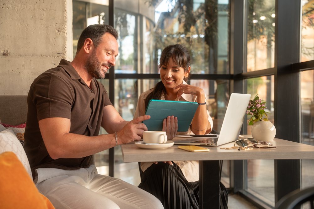 Two coworkers collaborate using a tablet and laptop in a sunlit office, business, coworker, Seville, Andalucia.