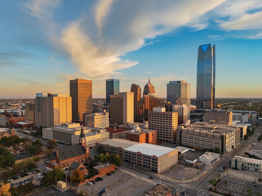 Oklahoma City skyline illuminated by orange Sunset light under a partly cloudy blue sky with urban buildings and a church with spires, Americana, Historic, USA.