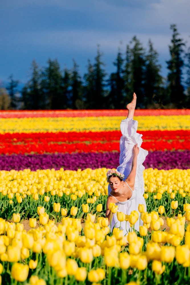 Ballet dancer in a white dress and flower crown poses barefoot in a vibrant tulip field, USA.