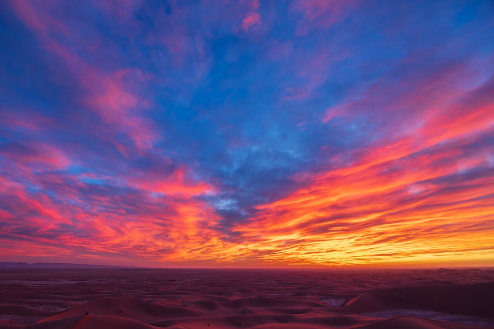 Colorful Sunrise over the Chaggaga Sand Dunes with clouds and an expansive desert landscape visible at the horizon, Lifestyle, Culture, Morocco.