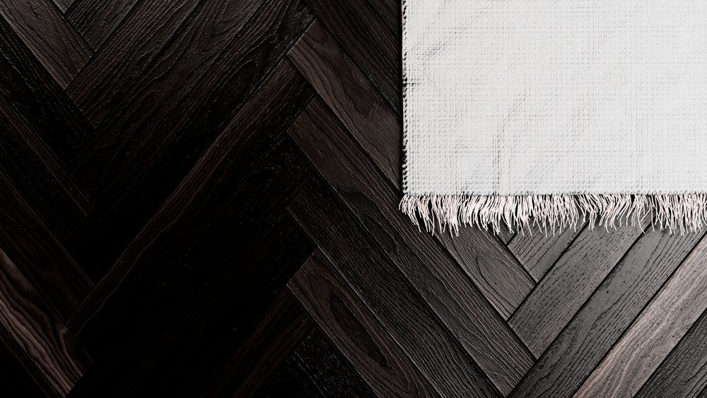 White textured woven rug with decorative fringe on dark wood parquet floor showing wood grain pattern.