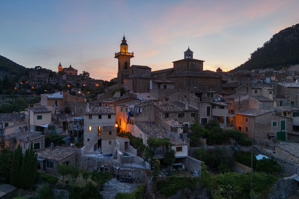 Skyline of Valdemossa village at Dusk showing illuminated church towers and stone houses among hills, Landscape, Lifestyle, Malloeca, Spain.