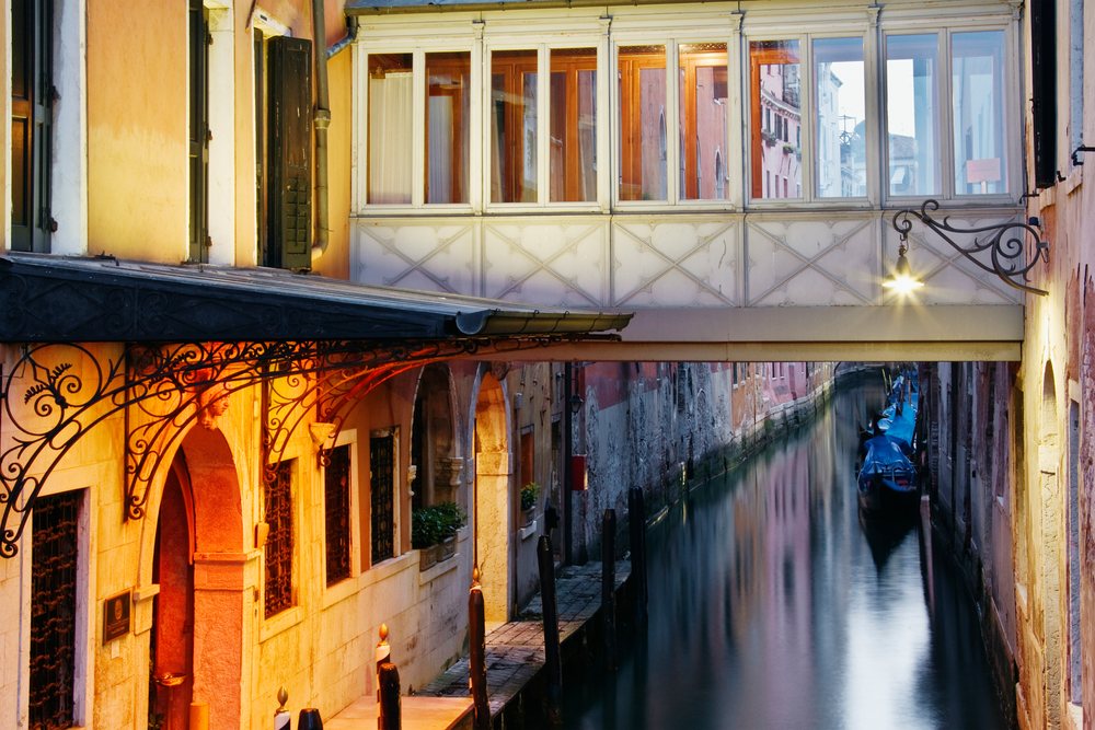 Veneto canal in Venice, with gondolas moored under a bridge between historic buildings at dusk, Italy.