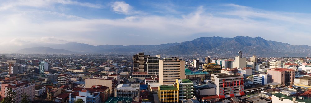 Panoramic cityscape of San Jose, showing urban buildings and distant mountains under a partly cloudy sky, Costa Rica.