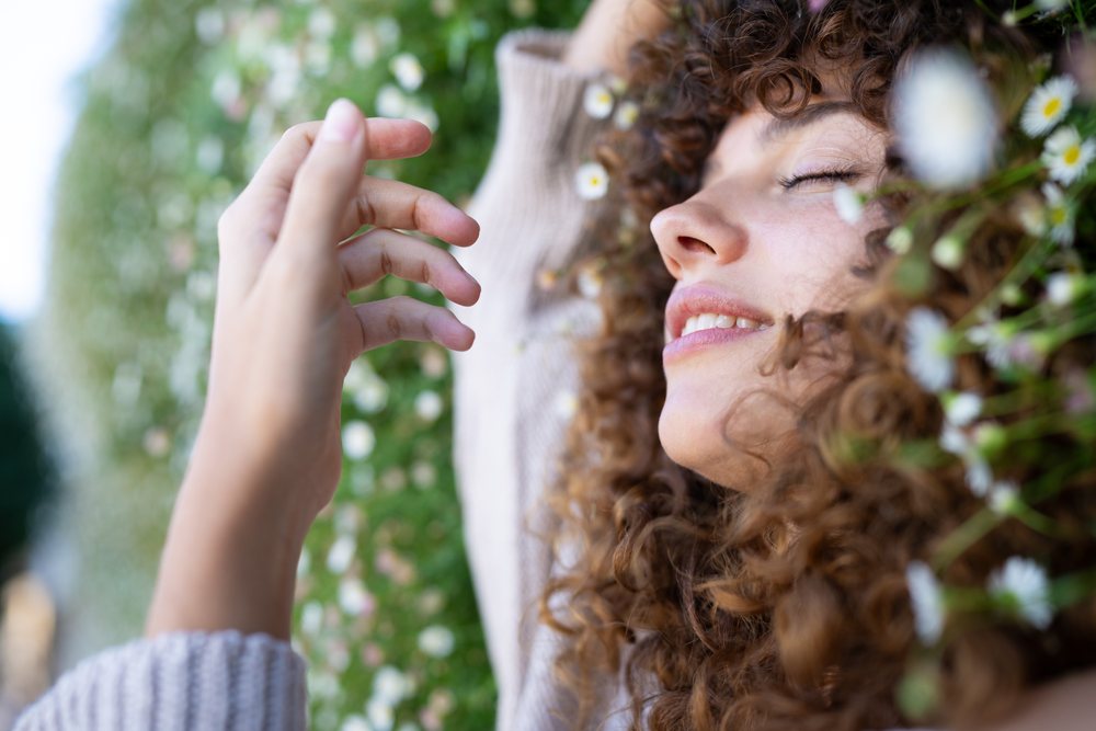 Woman with curly hair smiling peacefully seated among daisies in a garden, home story, influencer, Spain.