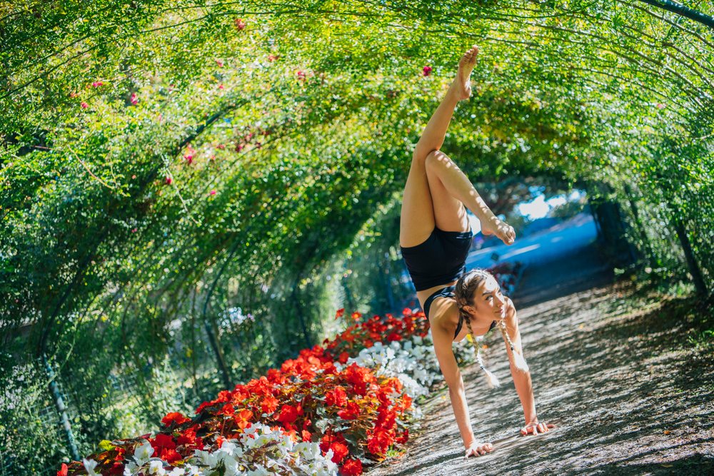 Woman performing a handstand under a green garden tunnel lined with red and white flowers, contortionist, Tacoma, WA, USA.