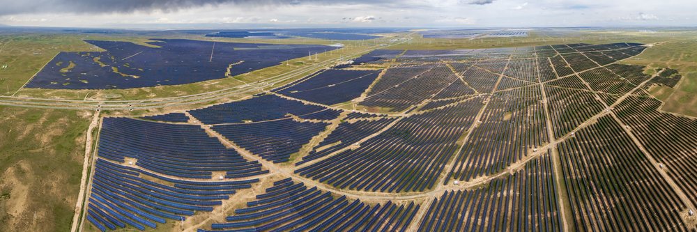 Solar Panels covering a large landscape with wind turbines in the background under a cloudy sky, Hainan - Xinghai, Qinghai Provinca, Anduo Tibet.