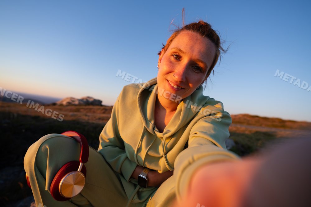 A young white woman in casual clothing takes a selfie outdoors