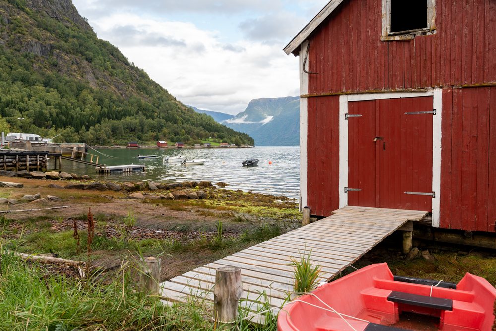 Red boathouse with white trim and a wooden dock beside a calm, coastal town, village, Luster, Fjord, Norway.