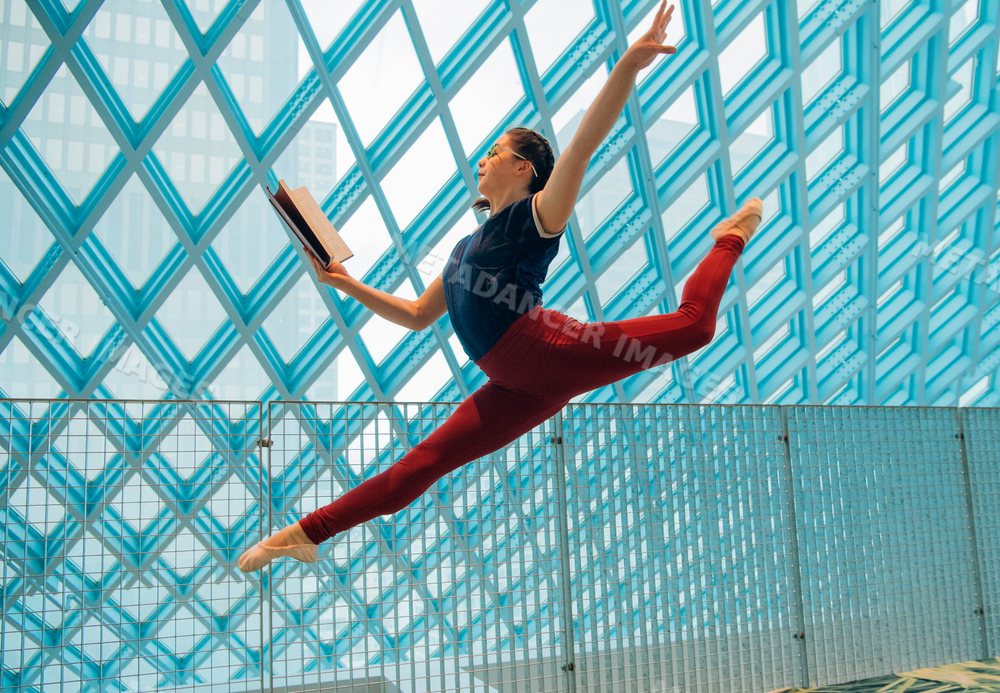 A female dancer leaps through the Seattle public library while reading