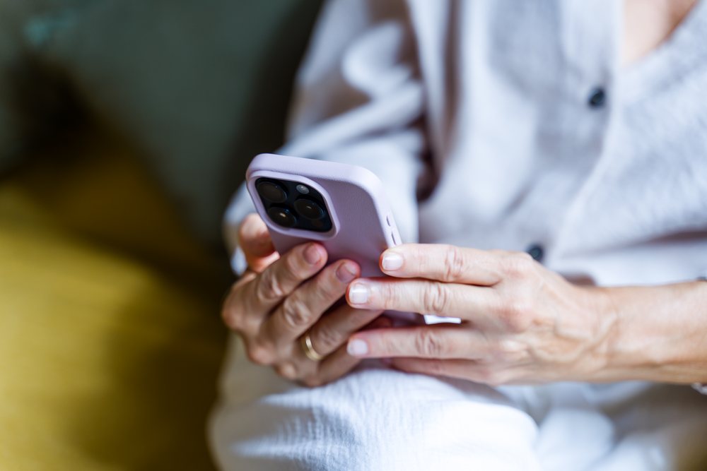 Adult hands holding a smartphone with a purple case indoors, using the touchscreen while wearing casual clothing, Spain.