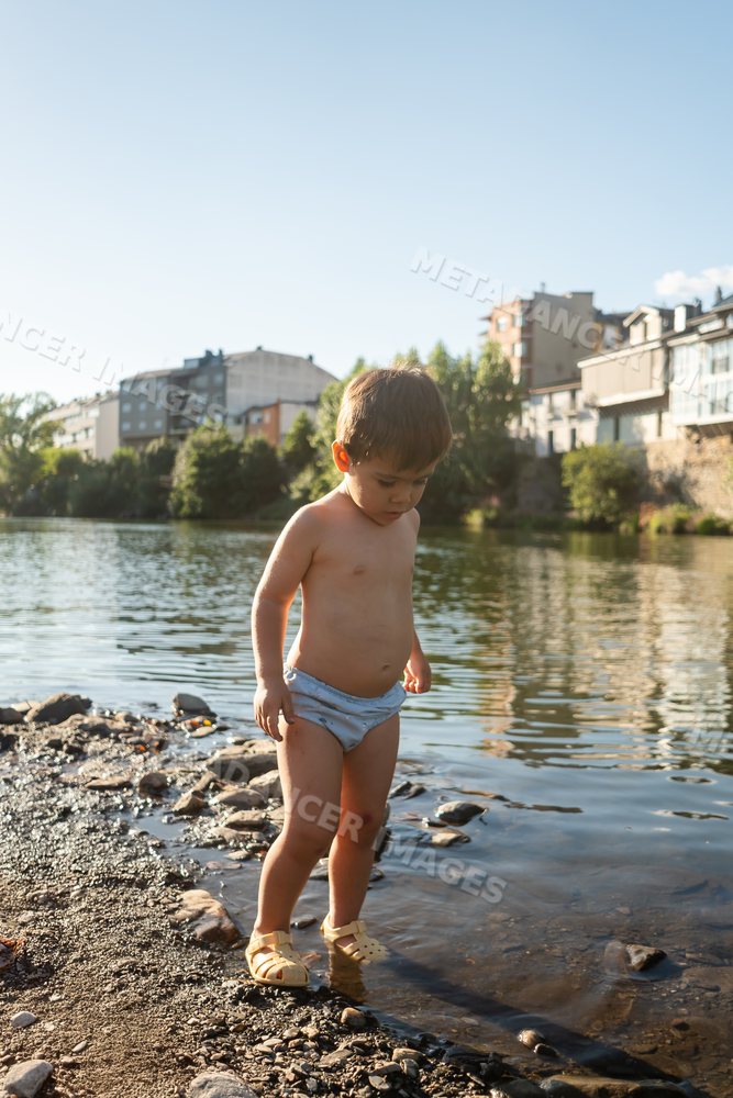 Toddler white boy exploring shallow riverbank water