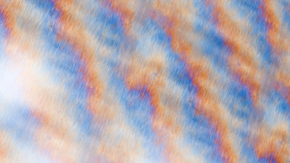 Close-up view of rust and oxidation patterns showing orange and blue discoloration on a metal surface.