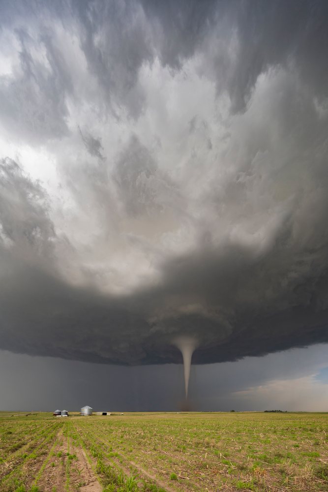 Tornado vortex funnel descends from storm clouds over a farm field with multiple grain silos, Dickens, Nebraska, USA.