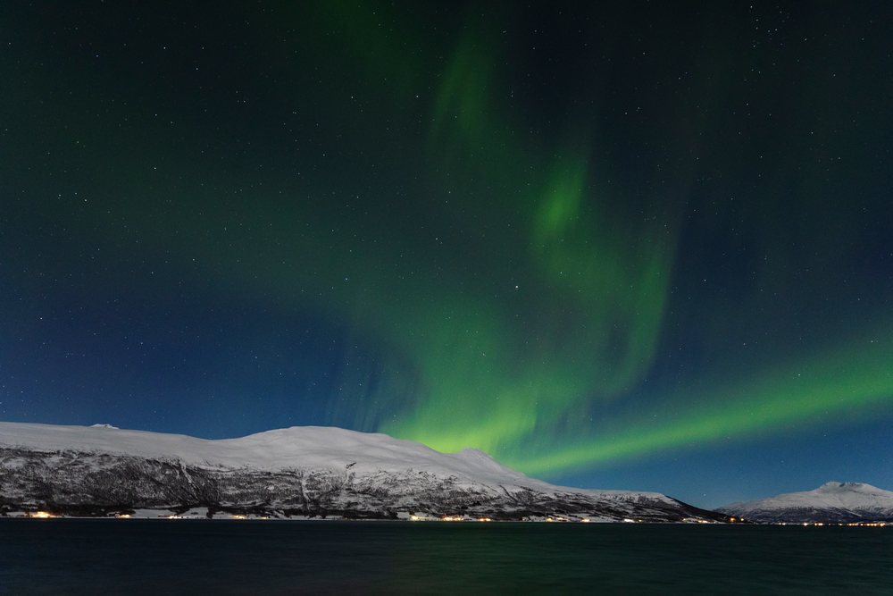 Northern Lights display glowing green in a starry night sky above snow-covered mountains and Balsfjorden fjord, Landscape, Mestervik, Norway.