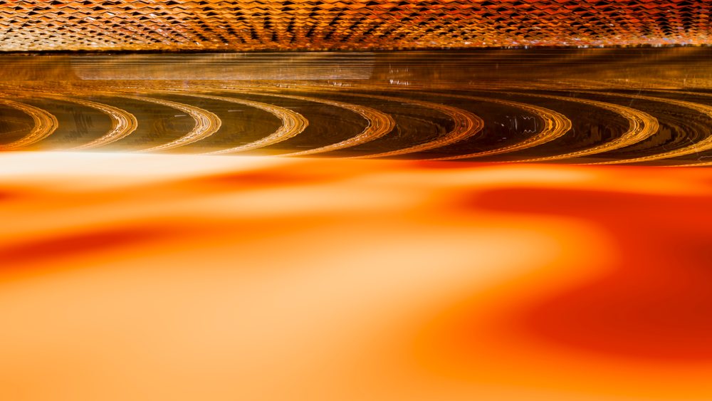 Orange liquid with wavy, reflective surface forming a warm-toned abstract pattern.