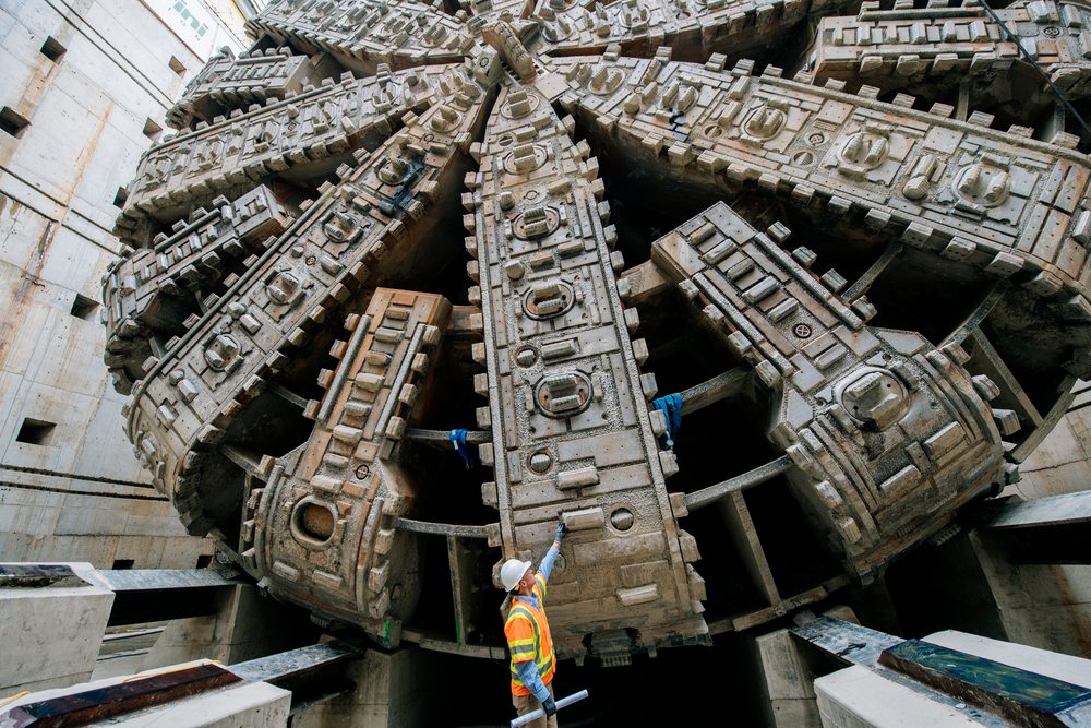 Construction worker inspects a massive tunnel boring machine at a construction site, Bertha, drilling, USA.