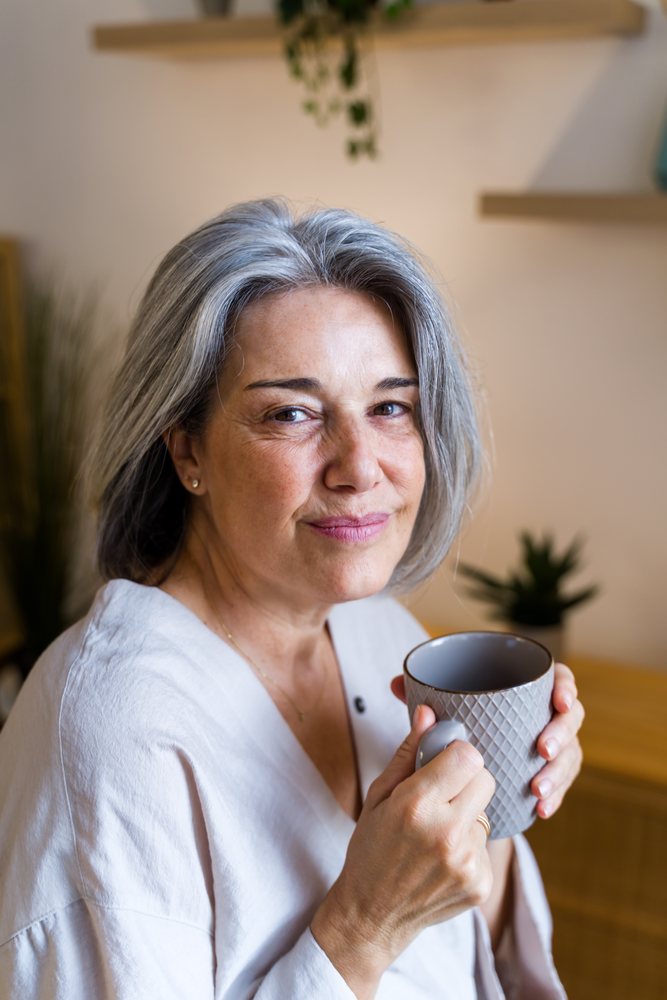 Woman with gray hair holding a gray ceramic mug indoors, Spain.