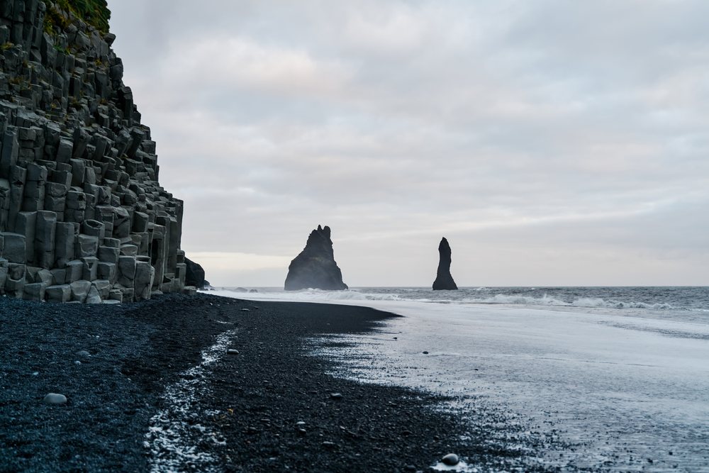 Basalt columns rise along a black sand beach with ocean waves