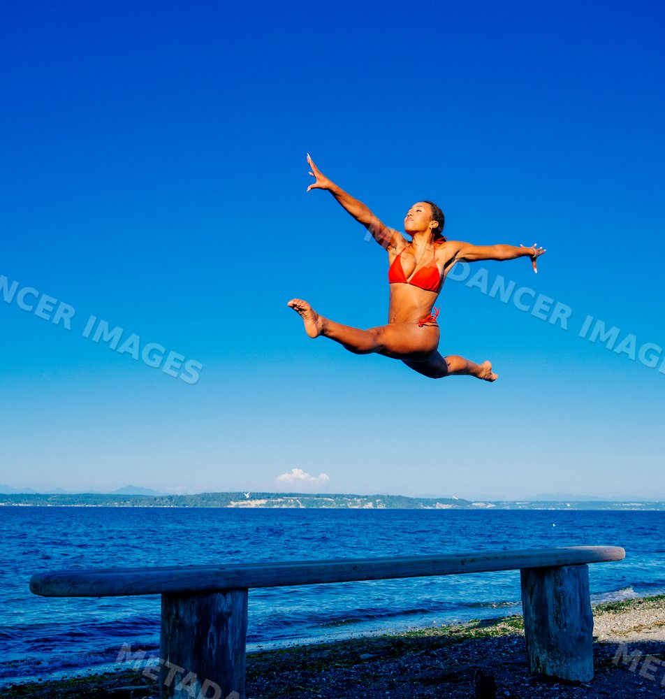 Woman jumping in split leap pose on beach in washington USA