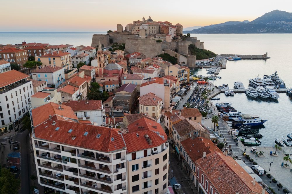 Citadel fortress overlooking the harbor with boats and red-roofed buildings at sunset, Travel Photography, Calvi, Corsica, France.