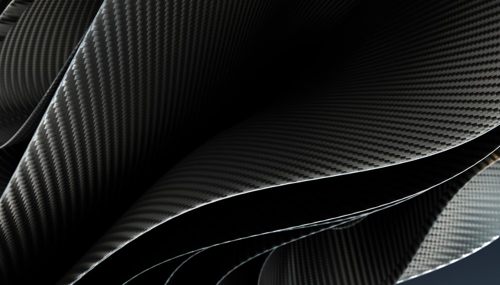 Closeup of folded carbon fiber sheets showing woven texture and curved surfaces with a dark, reflective finish and intricate weave patterns forming elegant curves and folds.