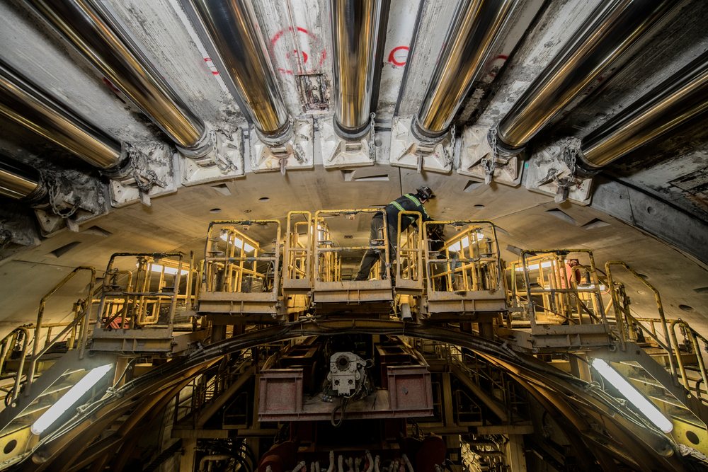 A construction worker inspects a drilling machine inside a tunnel during underground construction, USA.