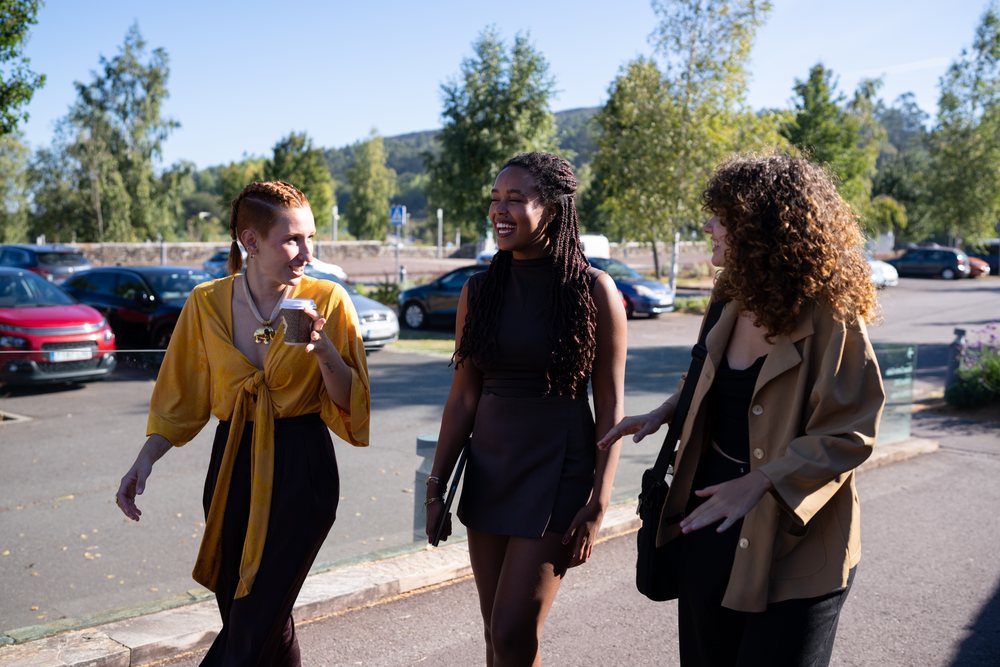 Three women walk and chat happily in a sunny parking lot, Spain.